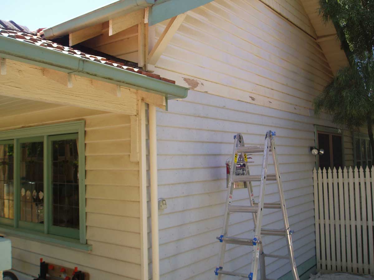 Weatherboard house exterior mid-prep with ladder, bare timber eaves