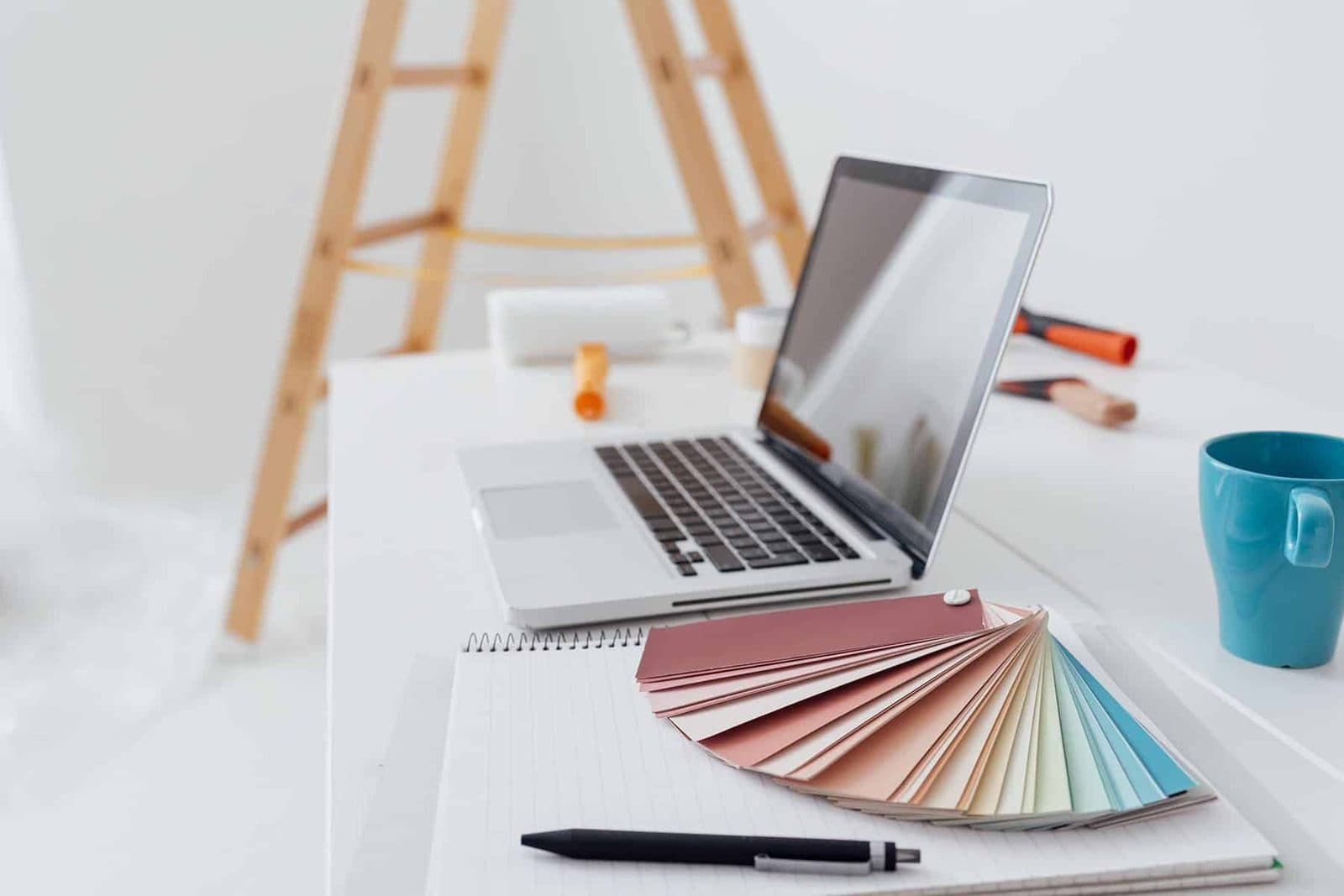 Laptop and paint colour fan deck on a desk while researching the right paint for the job